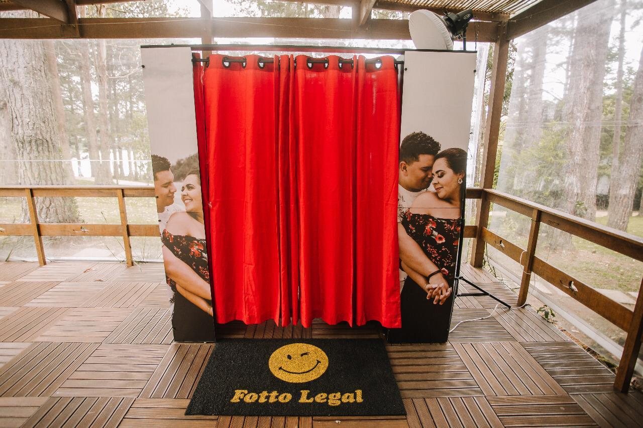Cabine de fotos Fotto Legal com cortina vermelha, painéis com a foto do casal e tapete com a logo